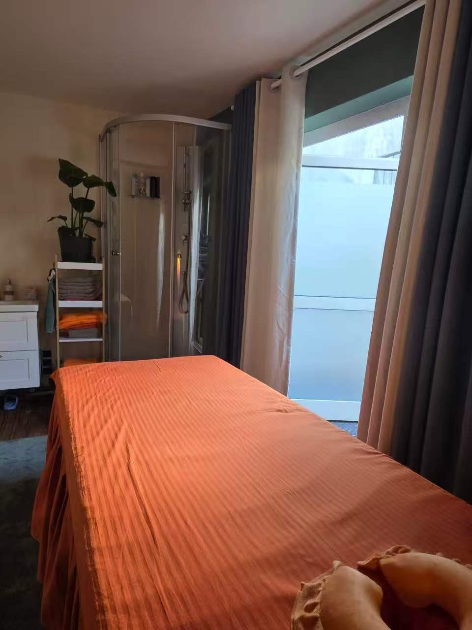 Behandlungsraum mit Massageliege, Dusche und Tageslicht am Fenster