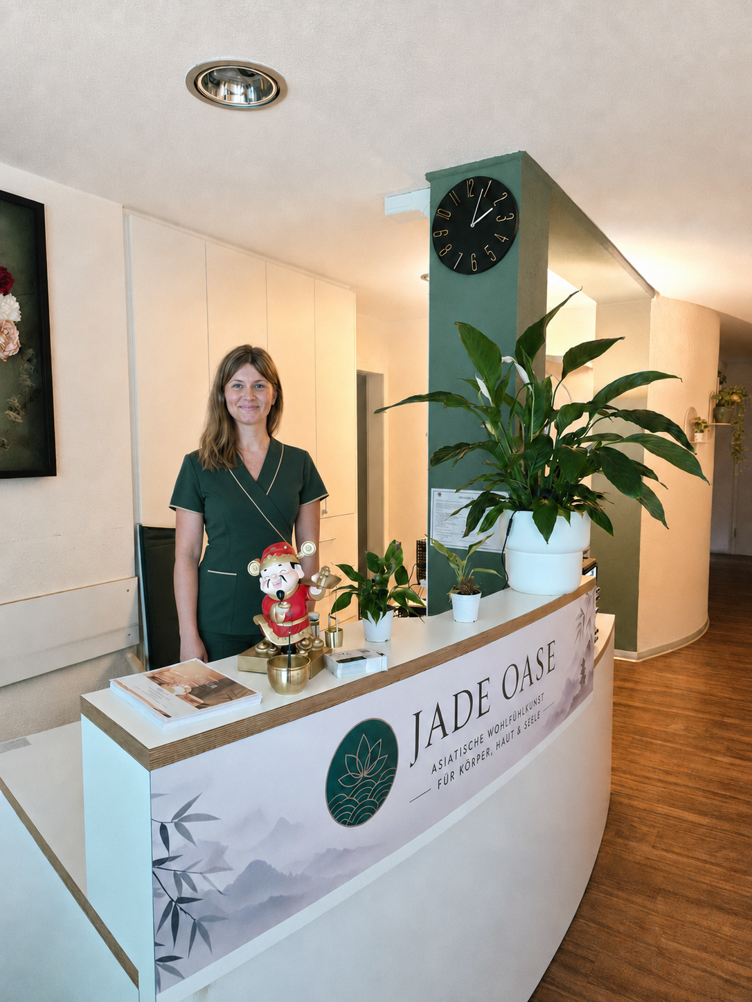 Mitarbeiterin der Jade Oase am Empfangstresen mit Markenlogo und grüner Wand